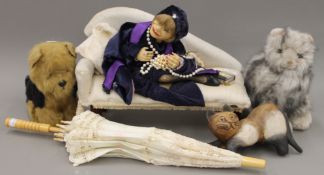 A doll on a miniature chaise lounge, two soft toys - a cat and a dog, a wooden cat and a parasol.