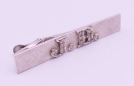 A silver and diamond tie clip with initials JB. 5 cm long, 0.8 cm high.