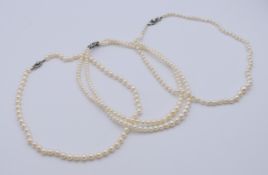 Two single strand pearl necklaces and a two-strand pearl necklace, two clasps marked 9 ct.