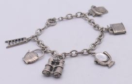 An unmarked white metal charm bracelet with various charms (ladder, kettle, binoculars, mirror,