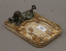 An onyx ashtray mounted with a cold-painted bronze of a young boy smoking. 18 cm long.