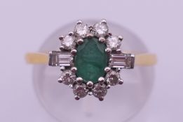 An 18 ct gold ring, centred with an oval emerald surrounded by ten diamonds. Ring size M. 4.
