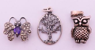A silver and amethyst butterfly brooch, a silver owl charm and a silver tree charm.