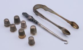A pair of silver sugar tongs, seven silver thimbles and a silver-handled button hook.