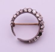 An unmarked gold, silver and diamond crescent brooch (with one loose stone). 2.5 cm diameter.