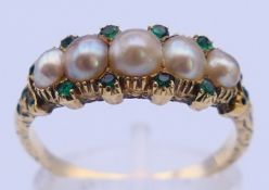 An unmarked gold, pearl and emerald ring. Ring size P. 3.6 grammes total weight.