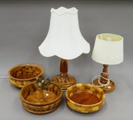 Two segmented wooden table lamps and three matching wooden bowls, one centred with a nut cracker.