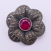 A silver and central red stone, possibly ruby, flowerhead brooch. 4 cm diameter.