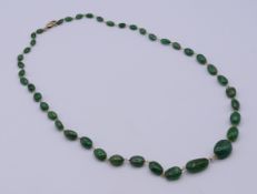 A graduated oval-shaped green stone necklace with silver gilt clasp. 60 cm long.