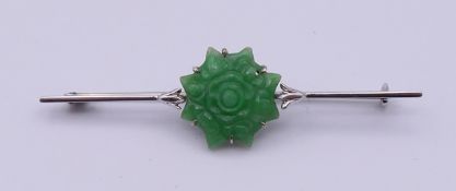 A 9 ct white gold and jade bar brooch. 6 cm long, jade central carving 1.5 cm diameter. 3.