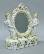A porcelain mirror surmounted with cherub. 27.5 cm high.