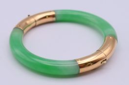An 18 K gold mounted jade bracelet. 5.5 cm internal diameter. 36.6 grammes total weight.