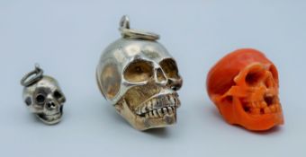 A carved coral skull and two silver skulls. The former 1.7 cm high.