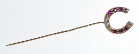 A 9ct gold horseshoe stick pin set with five square cut rubies and one paste replacement, 4.3g, 9.