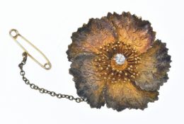 A yellow metal floral brooch/ pendant with textured matte finish set with an old cut diamond, 8.