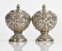 Pair of Indian or similar silver peppers with embossed decoration and screw stoppers to bases,