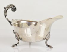 George V hallmarked silver sauce boat with shaped edge and scroll handle, raised on three feet,