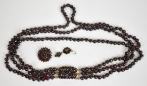 A triple strand garnet necklace with yellow metal clasp set with Bohemian cut garnets, a Bohemian