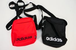Two Adidas small item shoulder bags, one red and one black, bags appear in unused condition.