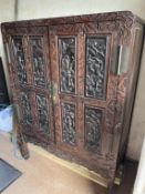 A carved hardwood twin door cabinet opening to reveal a shelved interior with two drawers,