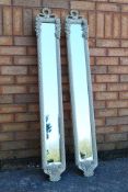A pair of slender wall mirrors with decorative foliate and floral frames and bevelled plates,