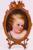 An oval portrait miniature on porcelain depicting a young child, in naturalistic wooden frame,