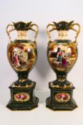 A pair of twin handled pedestal mounted vases decorated with transfer printed panels against a