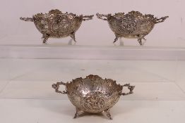 Three white metal, twin handled table salts with repousse decoration of putti and floral motifs,