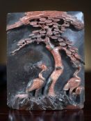 An antique Chinese variegated rouge jade carved relief panel depicting storks by a tree,
