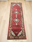 An eastern woolen rug on red ground, 258 cm x 77 cm.