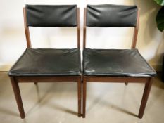 A pair of teak framed black vinyl dining chairs.
