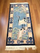 A Chinese woolen runner depicting storks in a landscape, 203 cm x 91 cm.