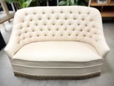 An early 20th century two seater salon settee in deep buttoned cream upholstery, width 117 cm.