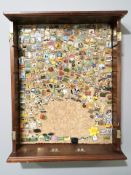 A mahogany framed cork board containing a large quantity of enameled lapel pins.