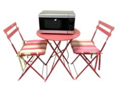 A metal folding circular patio table, two matching chairs and a microwave.