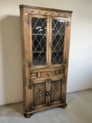 A reproduction carved oak standing corner cabinet with leaded glass doors,