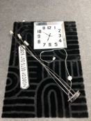 A contemporary machined black rug, a wall clock and a standard lamp.