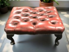 A Chesterfield deep buttoned oxblood leather rectangular footstool on ebonised cabriole feet,