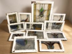 Twelve various 1930's stained and leaded glass windows in painted frames, largest 88 cm x 62 cm.