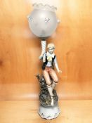 A large continental ceramic figural lamp depicting a boy sat on a log with large glass shade,