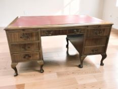 An early 20th century walnut twin pedestal seven drawer writing desk with red leather inset top,