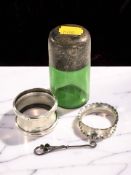 A green glass dressing table bottle with silver lid, a small button hook and two napkin rings.