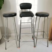 A metal framed high stool with black vinyl seat and two further similar stools.