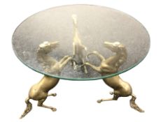 A circular glass topped coffee table supported by three brass rearing horses, diameter of top 60 cm.