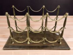 A brass bottle rack on wooden plinth, width 49 cm.