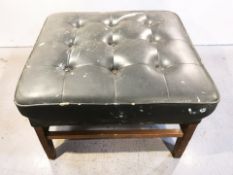 A 20th century teak and black vinyl footstool, in distressed condition, width 55 cm.