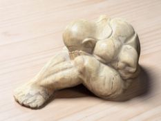 A carved wooden sculpture of a man with head clasped in hands, length 36 cm.