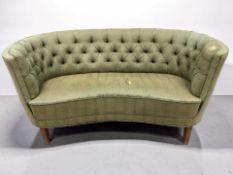 An early 20th century kidney shaped two seater salon settee in buttoned green upholstery,