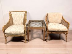 Two faux bamboo and caned armchairs, and a further glass topped lamp table.
