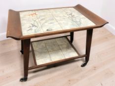 A continental walnut tile inset two tier trolley decorated with fish, length 80 cm.